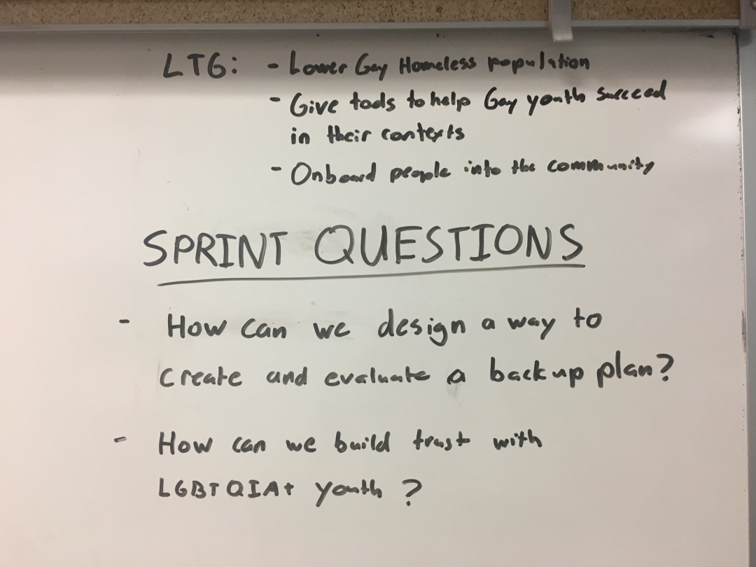 Sprints questions written on a whiteboard: 'How can we design a way to create and evaluate a backup plan?' and 'How can we build trust with LGBTQIA+ Youth?'